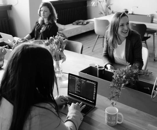 Three women collaborating around a laptop in an office environment